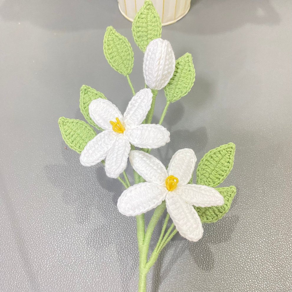 Crocheted white jasmine flowers with green leaves on a textured background