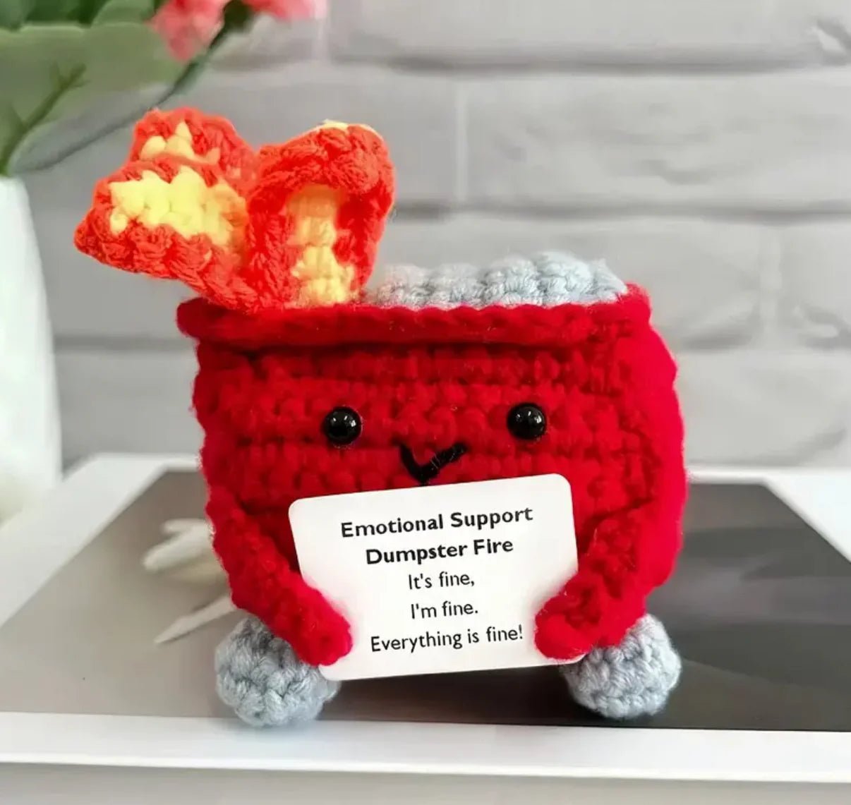 Crocheted red dumpster fire with "Emotional Support" sign, looking cute and stressed