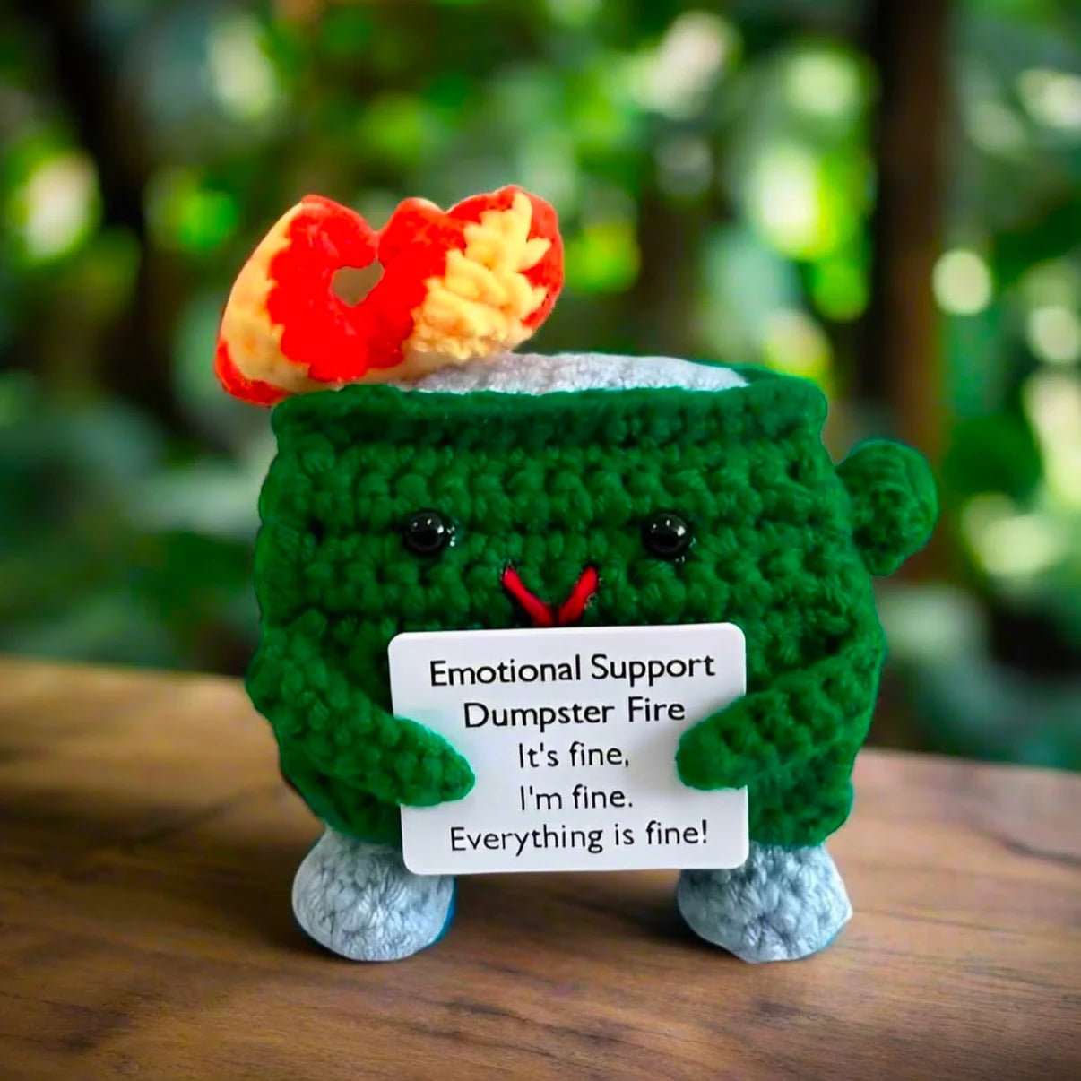 Crocheted green dumpster fire plush with "Emotional Support" sign, looking stressed but cute