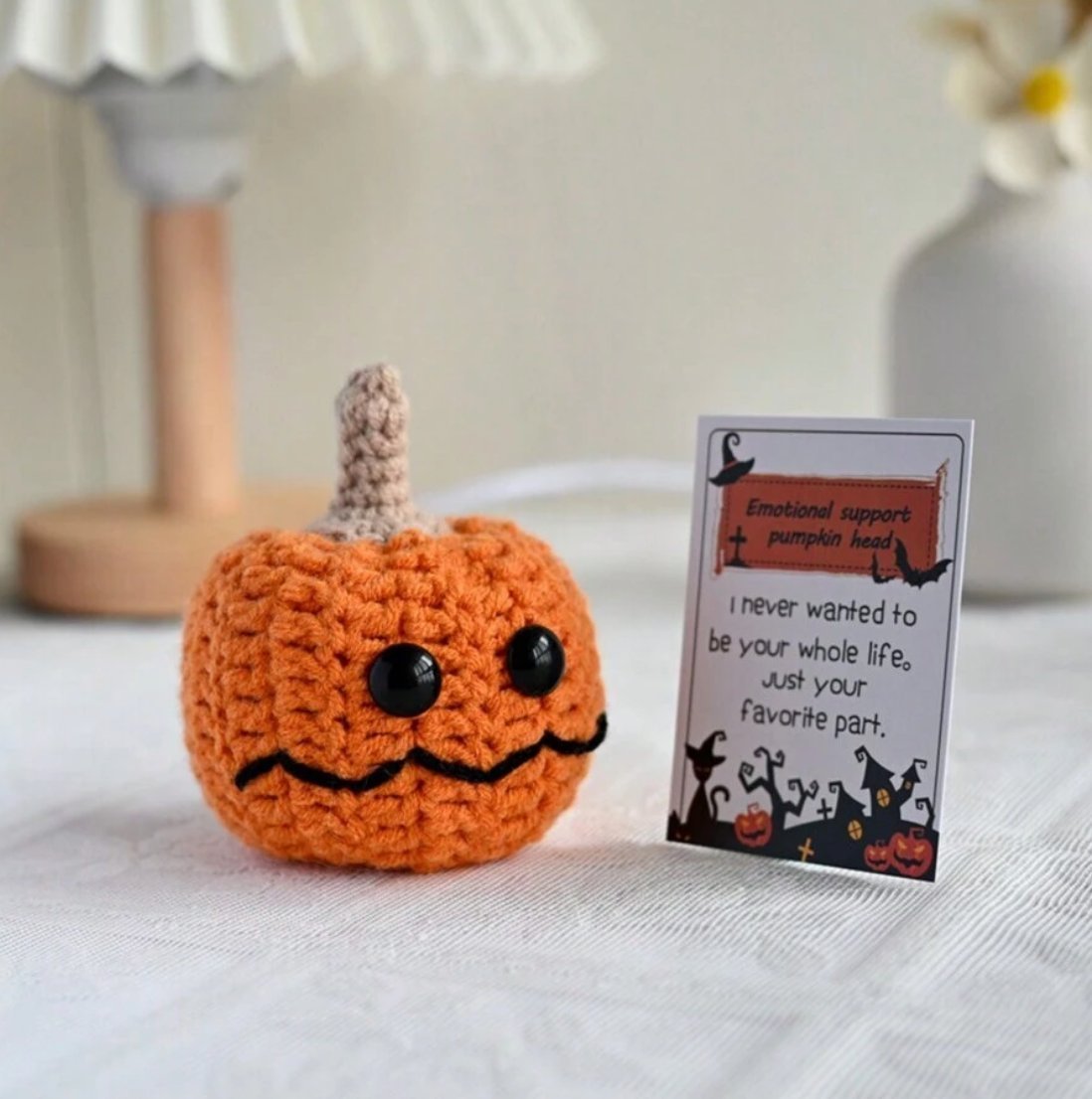 Crocheted orange pumpkin with googly eyes next to a humorous Halloween greeting card