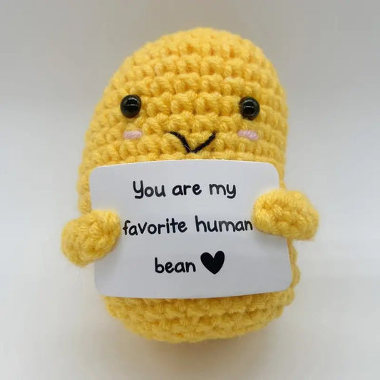 Yellow crocheted bean character holding a sign saying "You are my favorite human bean ❤️"