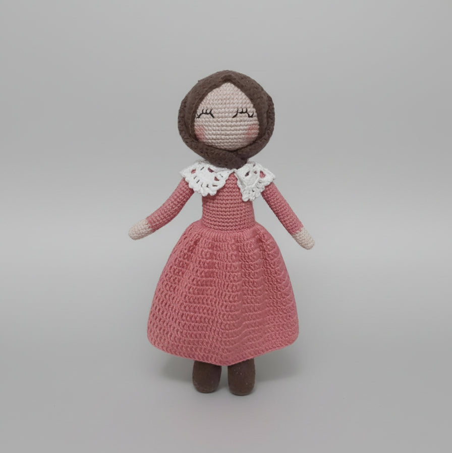 Crocheted doll in pink dress with white lace collar, standing against neutral background