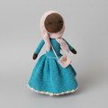 Crocheted doll in teal dress with pink hood and matching purse, standing against gray background