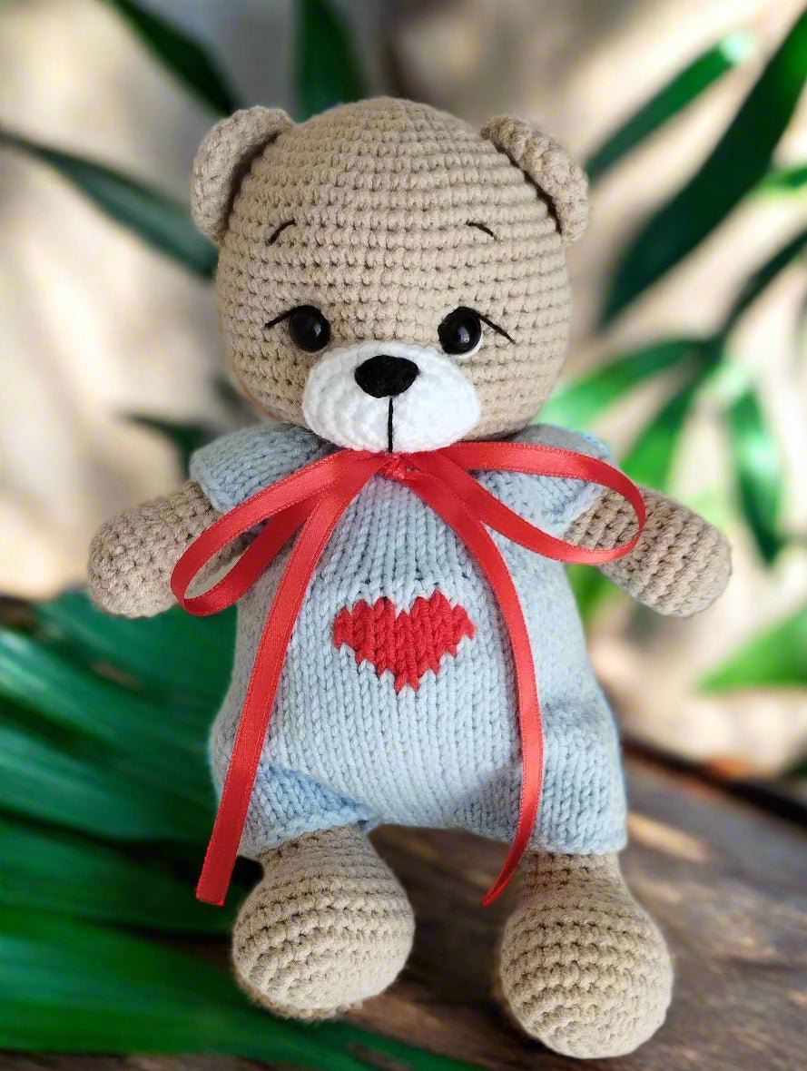 Crocheted teddy bear with blue sweater, red heart, and bright red ribbon bow