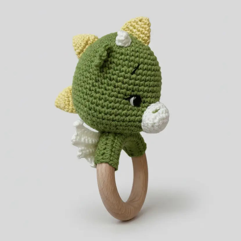 Green crocheted dinosaur baby rattle with wooden teething ring on white background