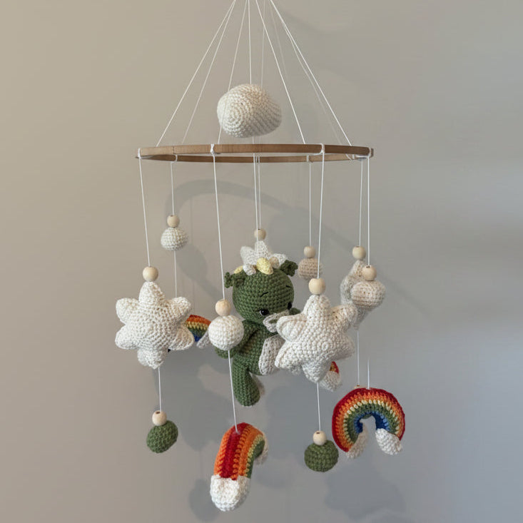 Crocheted mobile with various shapes hanging from a rod against a neutral background