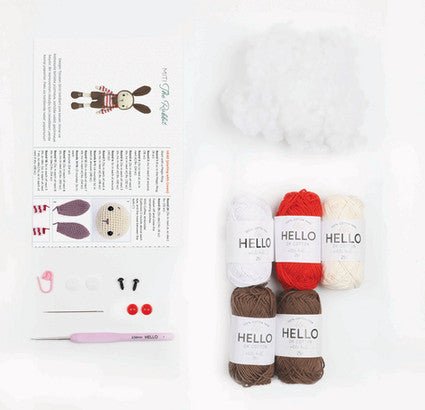 Knitting pattern and yarn skeins with "HELLO" labels in white, red, and brown colors.