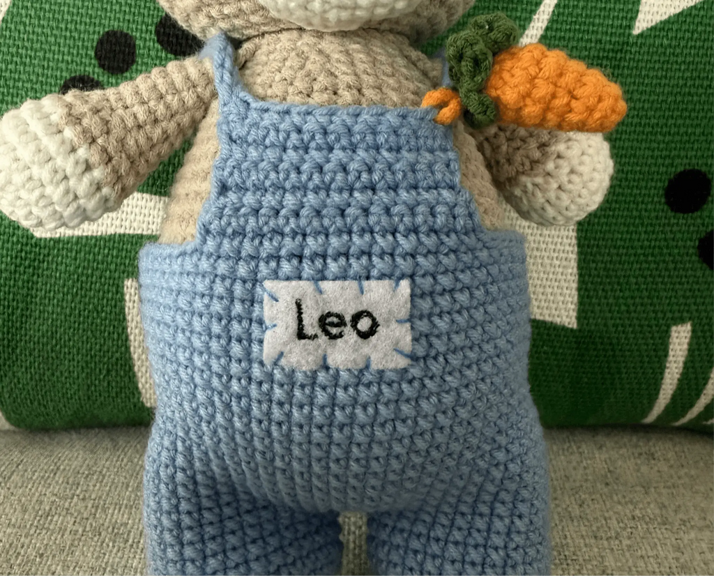Crocheted blue character with "Leo" name tag and orange carrot detail
