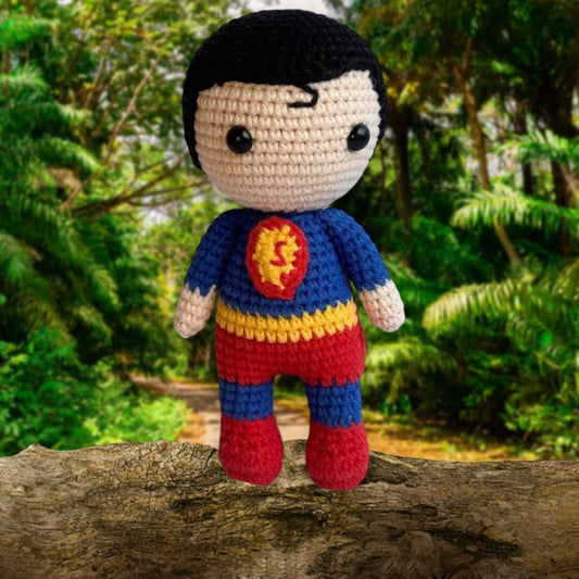 Crocheted superhero doll with blue, yellow, and red costume standing on a log in forest