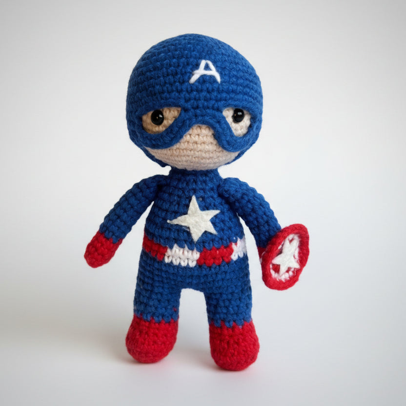 Crocheted superhero doll in blue and red, standing on a tree branch in a forest.