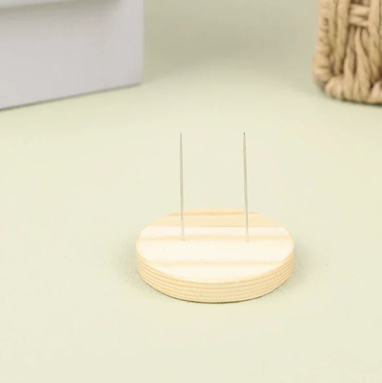 Two thin metal pins standing upright in a round wooden base on a light surface.