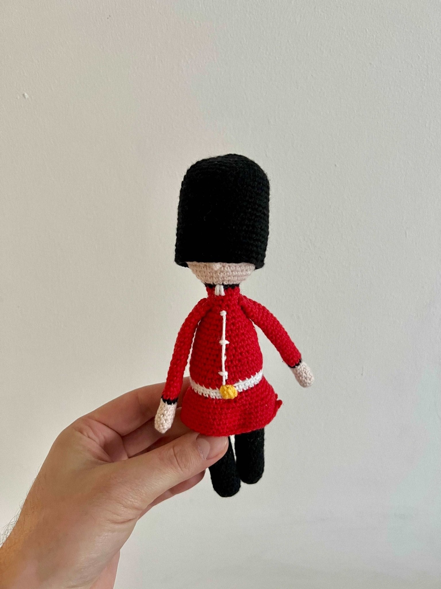 Crocheted Royal Guard figurine in red uniform and black bearskin hat, held by a hand