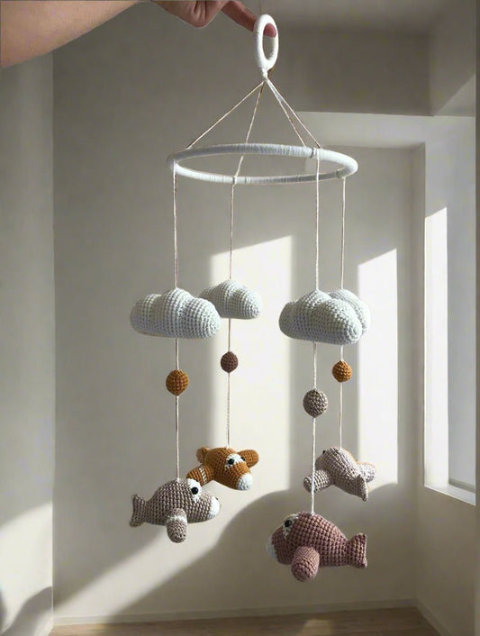 Handmade crocheted baby mobile with clouds, balls, and fish hanging from a white ring