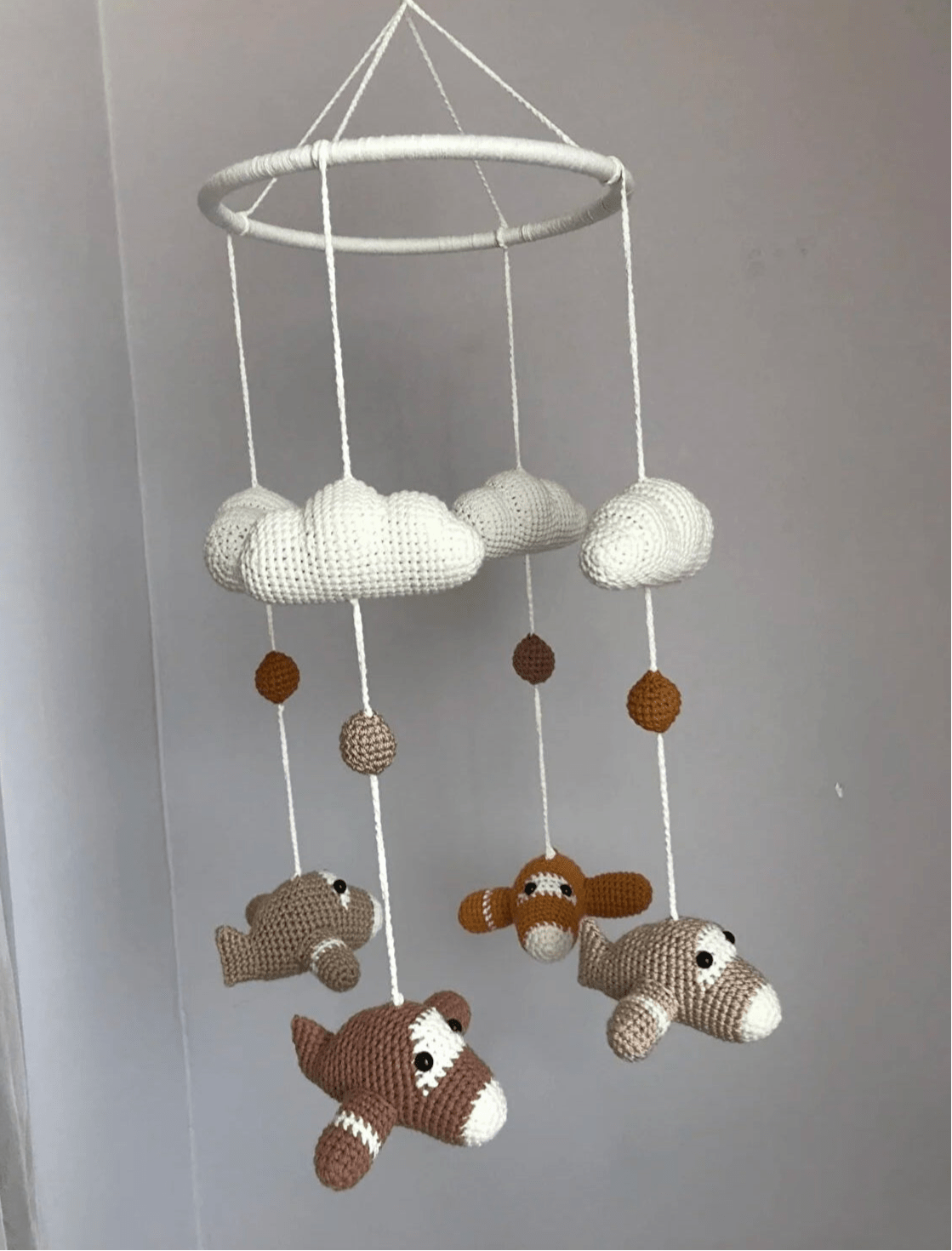 Crocheted baby mobile with clouds and airplanes hanging from white circular frame