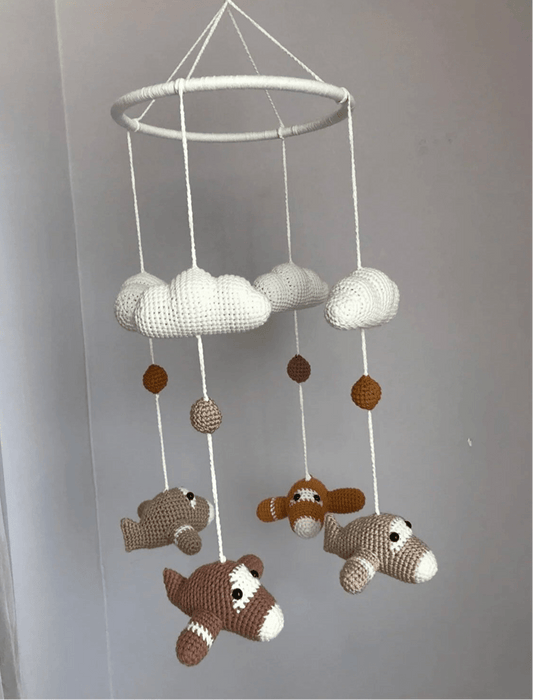 Crocheted baby mobile with clouds and airplanes hanging from white circular frame