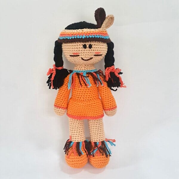 Crocheted doll in orange dress with braids and colorful fringe, smiling and standing