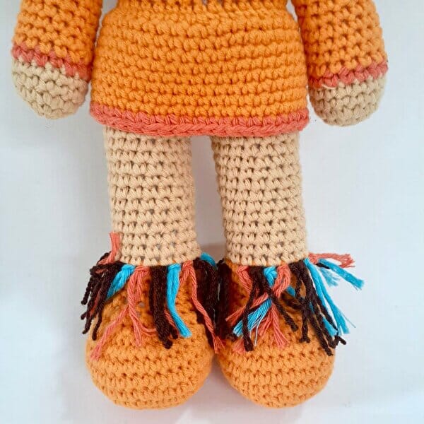 Crocheted doll legs in orange and tan, with colorful tasseled feet and trim