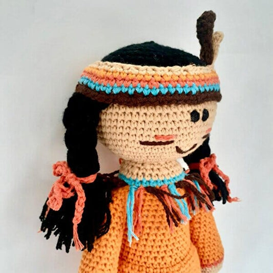 Crocheted doll with black braids, headband, and orange sweater, smiling sweetly