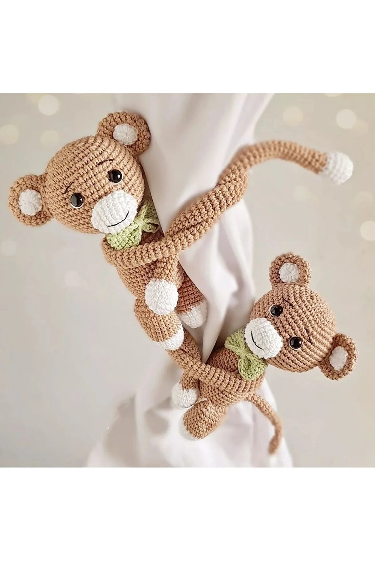 Two crocheted teddy bears with green bow ties, hanging on a white curtain.