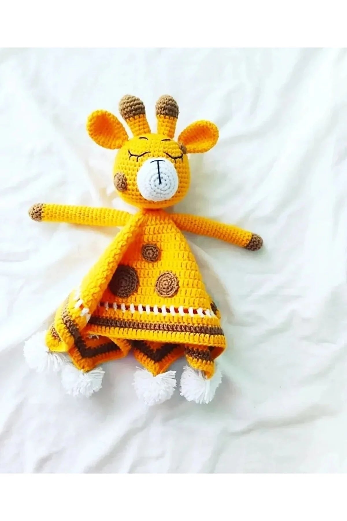 Crocheted yellow giraffe toy with brown spots and closed eyes on white fabric