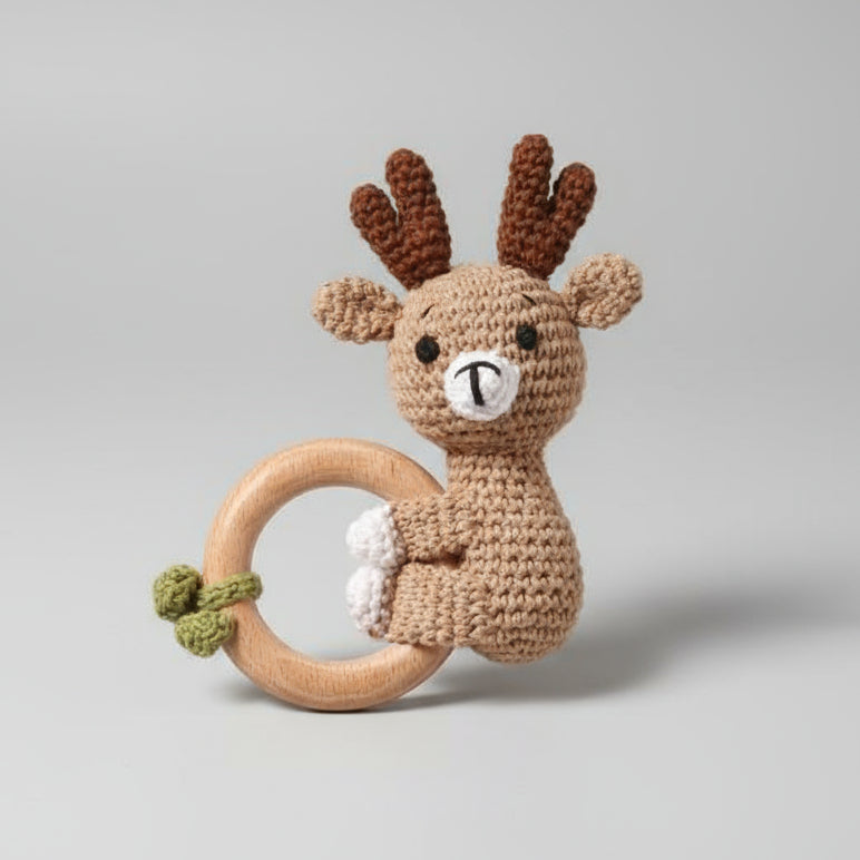 Crocheted deer baby rattle with wooden teething ring on gray background