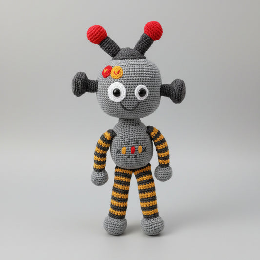 Crocheted robot toy with red antenna and striped yellow-gray limbs, smiling with white eyes