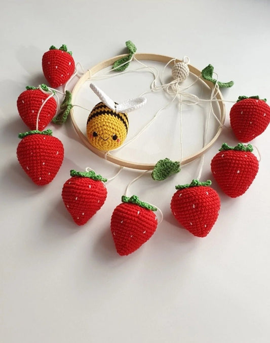 Crocheted red strawberries and a yellow bee around an embroidery hoop with strings